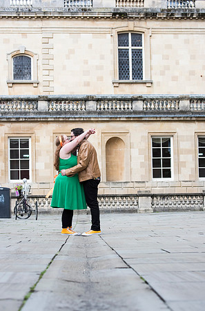 couple holding arms on their engagement day. Picture taken outside The Roman Baths and The Abbey in Bath.