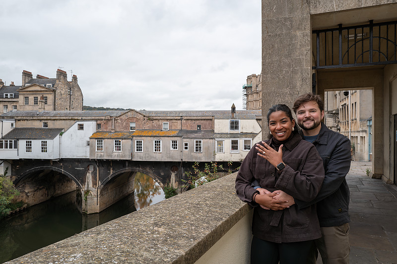 Engagement & Proposal pictures. Bride to be shows her ring with a groom to be behind her in Bath. View of the Pulteney Bridge in Bath