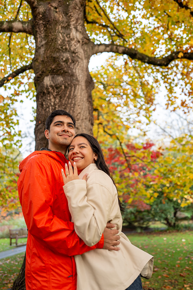 Woman showing her ring and the couple is looking away towards the future on their engagement in Bath. Botanical Gardens