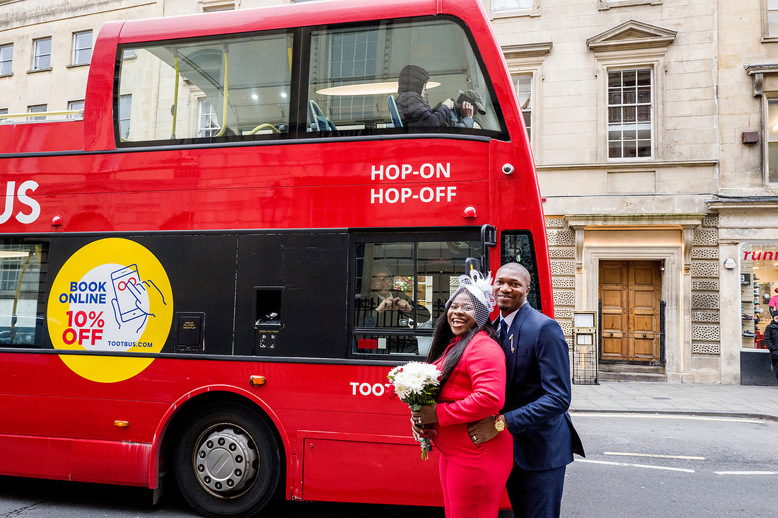 Bride and Groom standing outside the Guildhall. The bus stands behind them and a driver makes a shape of a heart. 